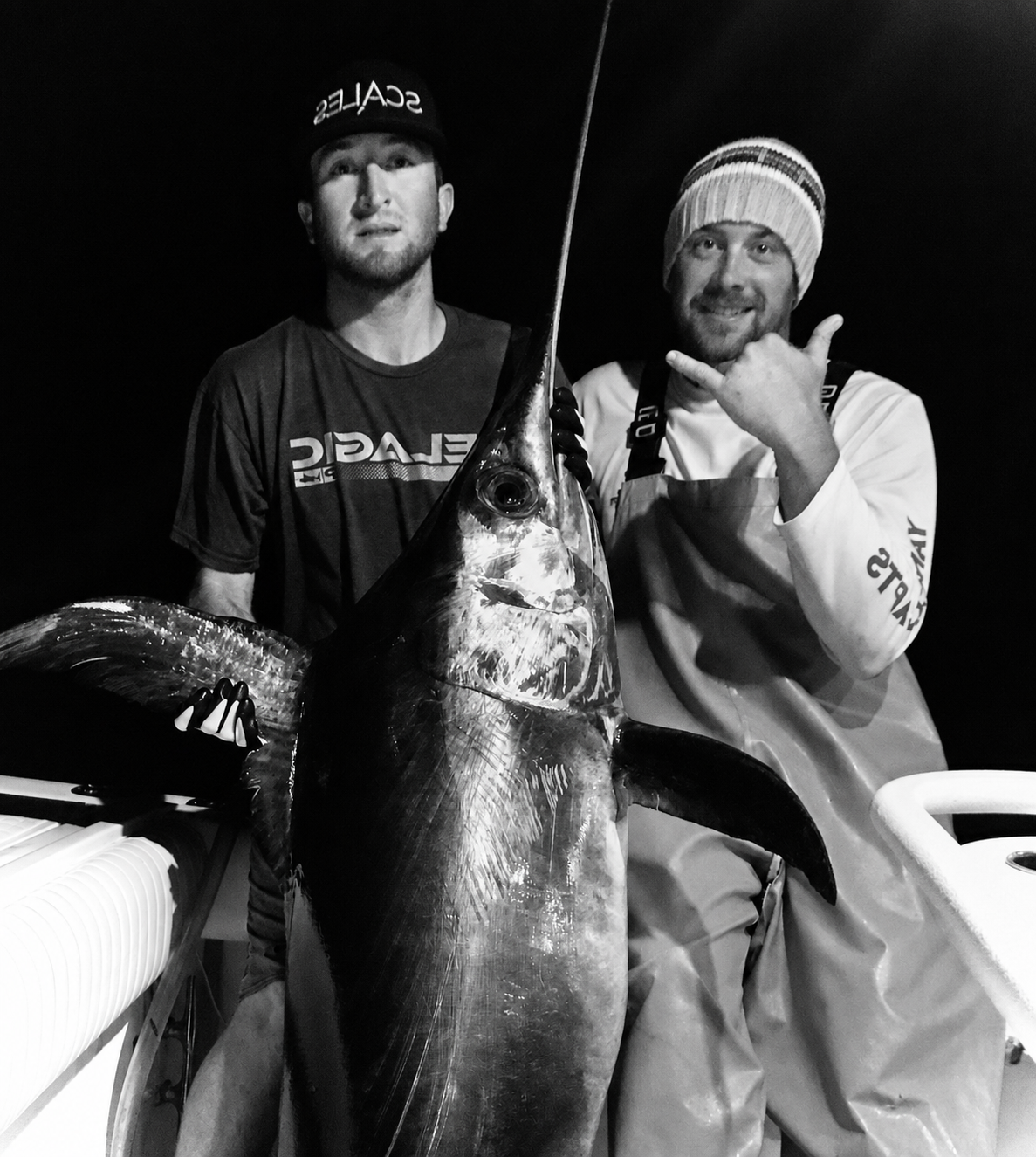 Two fishermen aboard an offshore boat in Florida at night with a large swordfish after the catch.