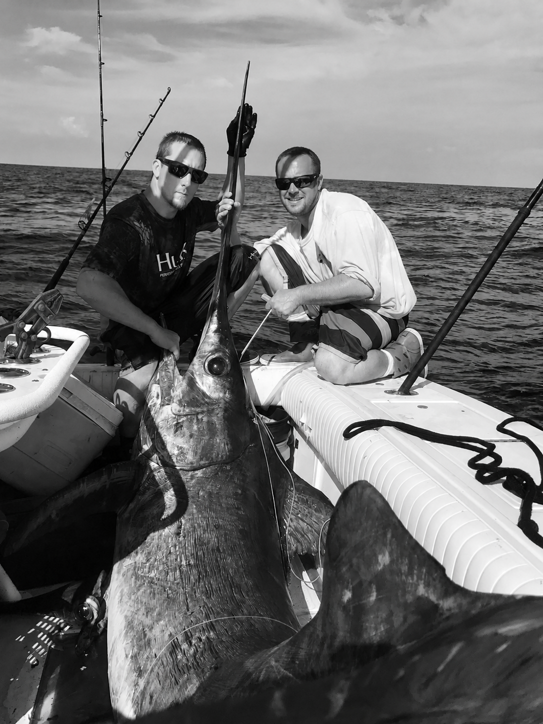 Two fishermen aboard an offshore boat in Florida with a very large swordfish on deck.