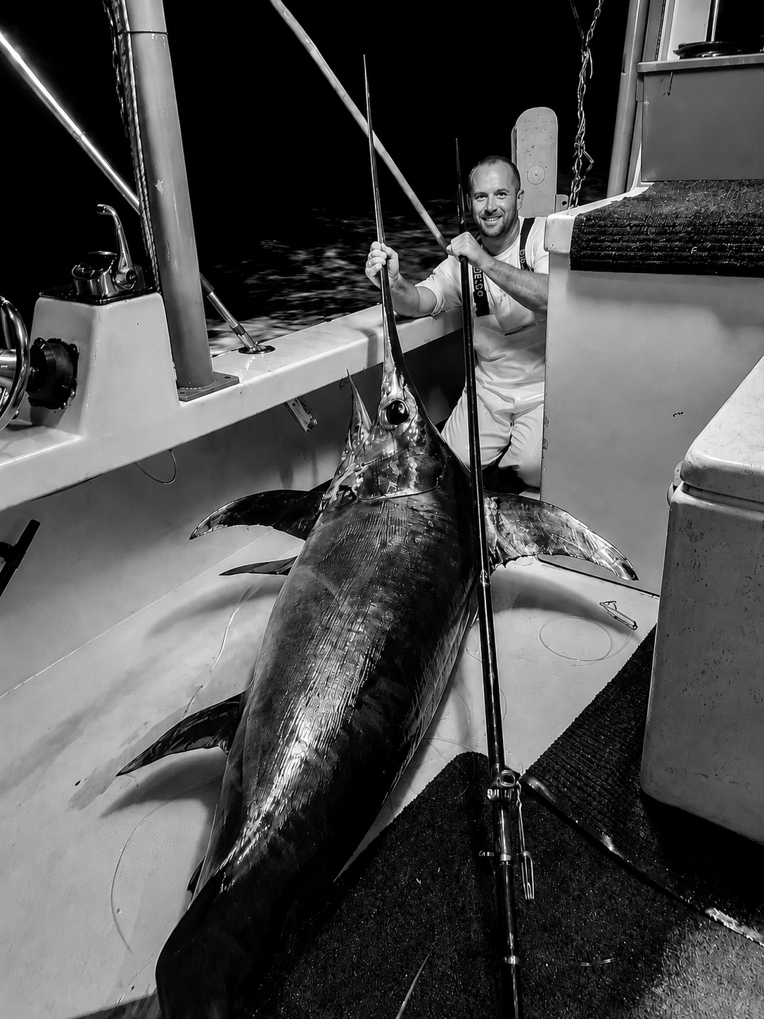 Fisherman aboard an offshore boat in Florida at night with a large swordfish on deck.