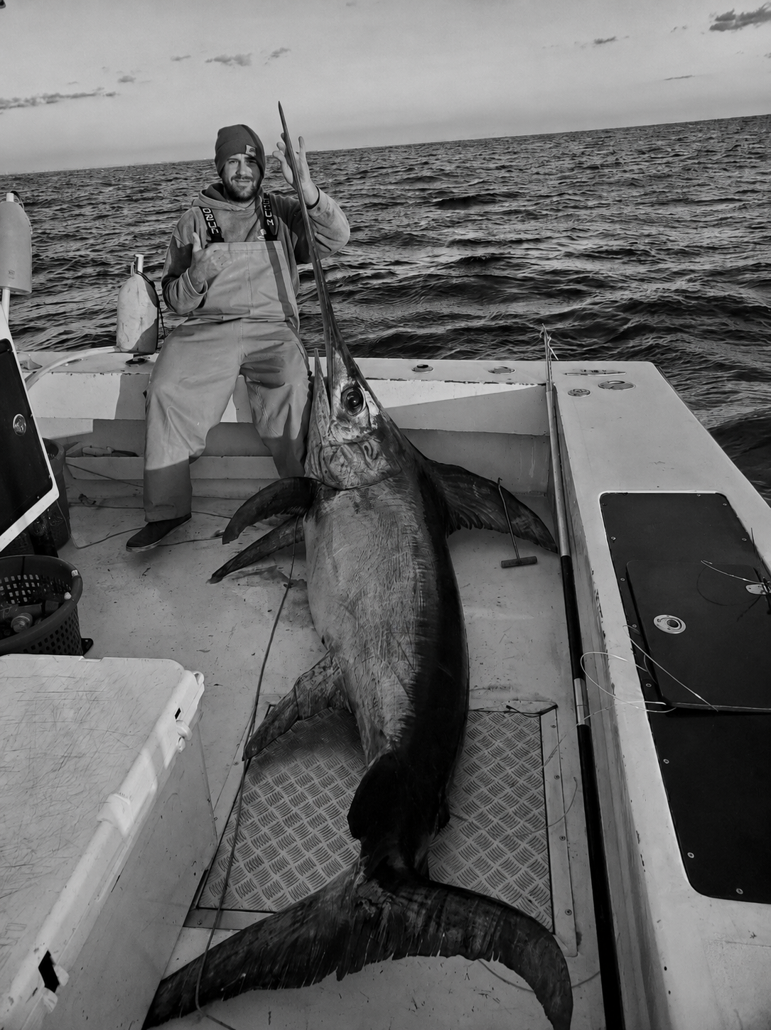 Fisherman aboard an offshore boat in Florida beside a giant swordfish stretched across the deck at sea.