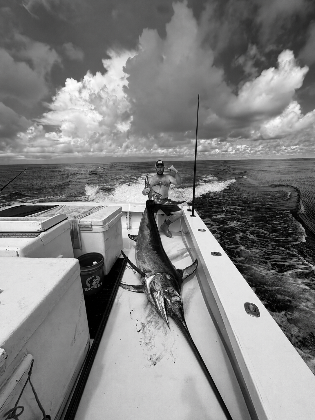 Fisherman aboard an offshore boat in Florida with a large swordfish stretched along the deck under dramatic open-water skies.