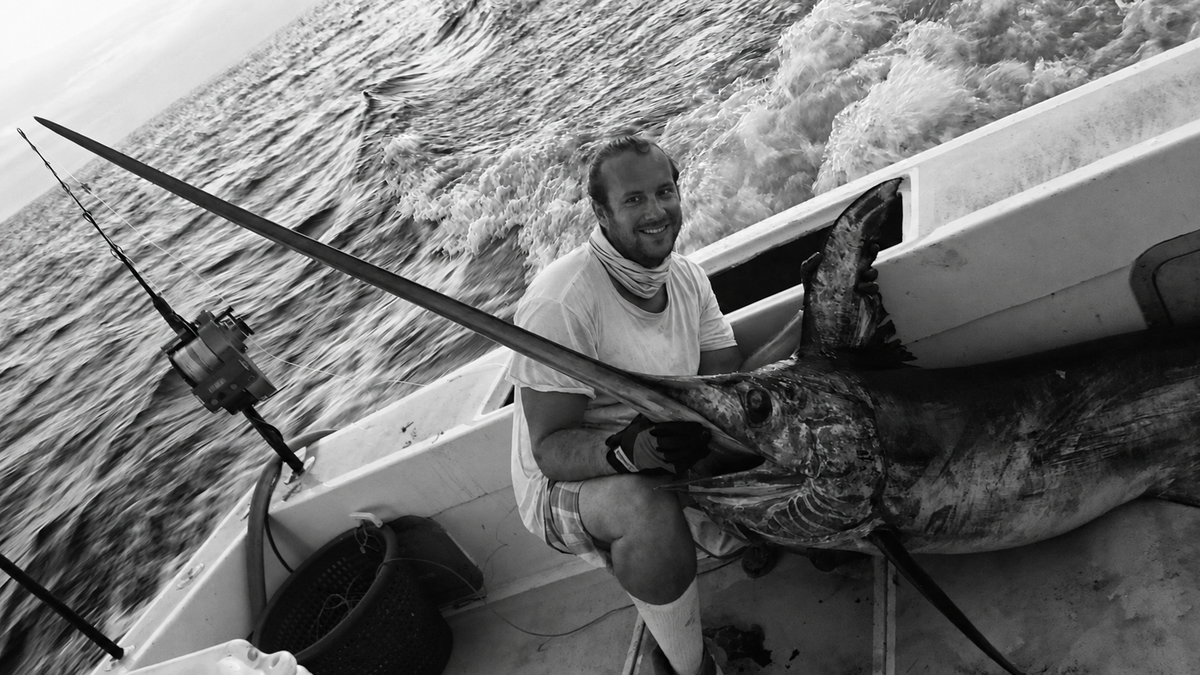 Fisherman aboard an offshore boat in Florida beside a large swordfish at sea.