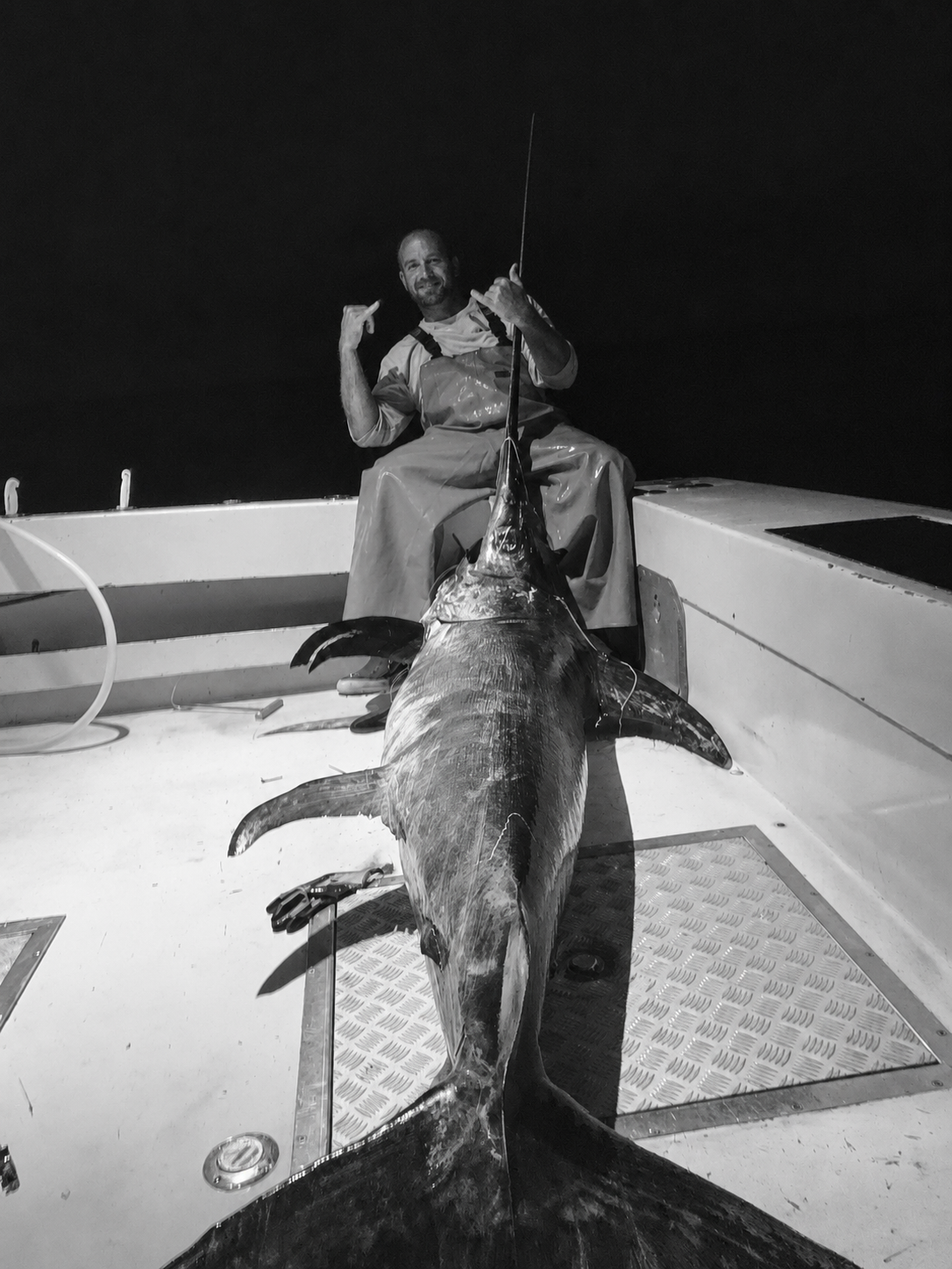 Fisherman celebrating aboard an offshore boat in Florida at night with a large swordfish stretched across the deck.