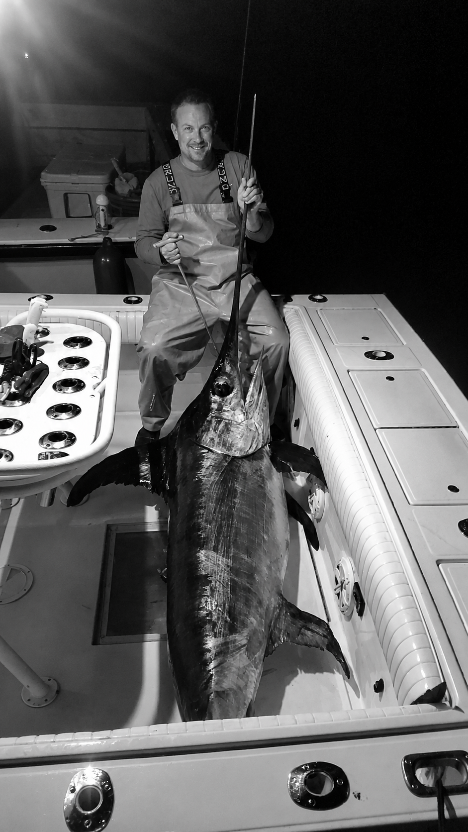 Fisherman aboard an offshore boat in Florida at night with a large swordfish laid out on deck.