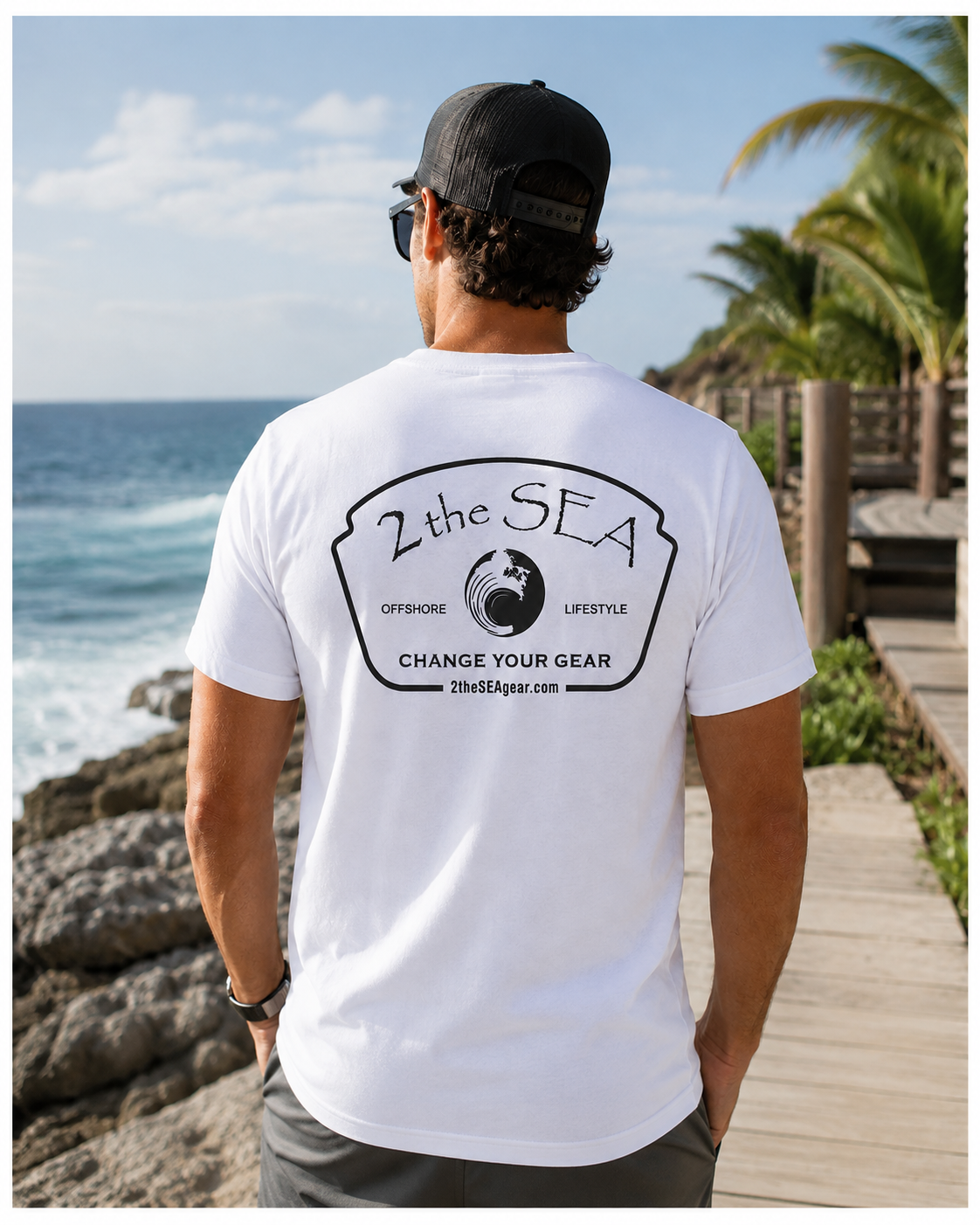 Back view of The Mark white 2theSEA T-shirt featuring the black Change Your Gear badge graphic beside a tropical ocean shoreline.
