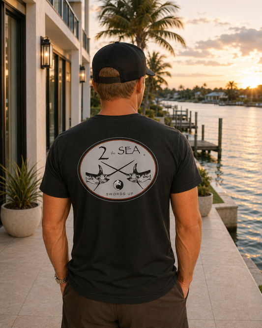 Back lifestyle view of The Crossing Black 2theSEA T-shirt featuring the crossed-swordfish graphic in a refined waterfront setting.