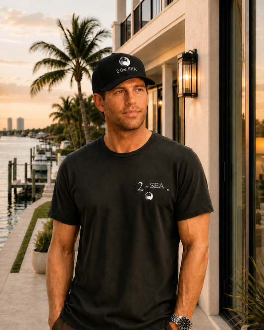 Front lifestyle view of The Crossing Black 2theSEA T-shirt featuring the small 2theSEA chest graphic in a waterfront setting.