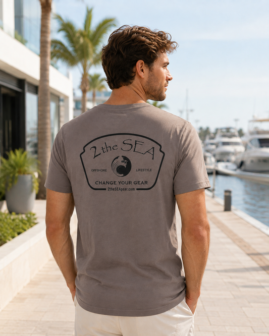 Back lifestyle view of The Mark Pebble Brown 2theSEA T-shirt featuring the large black Change Your Gear badge graphic in a marina setting.
